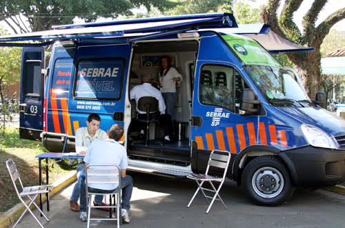 Veículo modelo Van na cor azul, customizada para atendimento móvel ao empreendedor. Na imagem constam pessoas sendo atendidas  